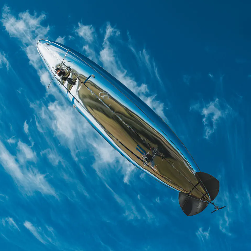 An unmanned airship with a reflective, silver hull surface, photographed from below. The earth's reflection is visible on the hull.